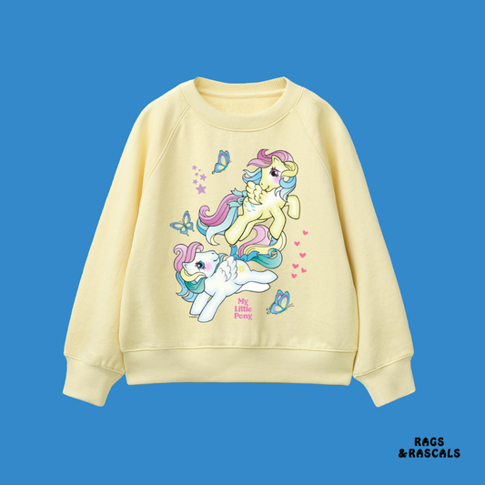 light yellow sweatshirt with cartoon pony design on a blue background, featuring the brand 'Rags & Rascals'.
