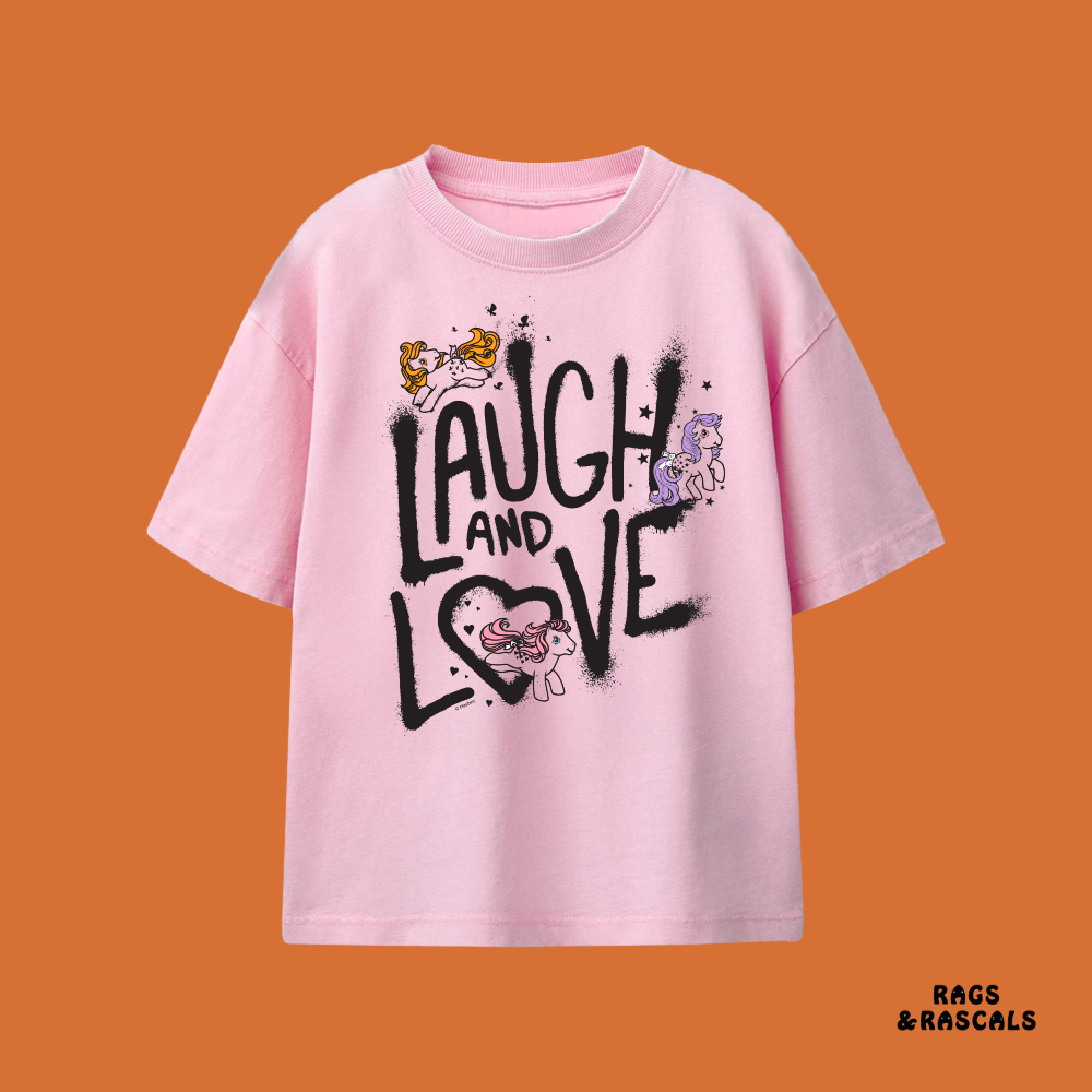 Pink t-shirt with 'Laugh and Love' text and cartoon characters on an orange background,  from a brand called 'Rags & Rascals'.